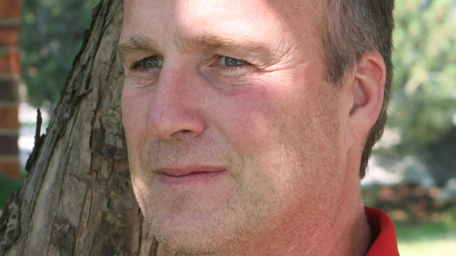 Headshot of Channing Schneider. There is a man with a red shirt looking to the side.
